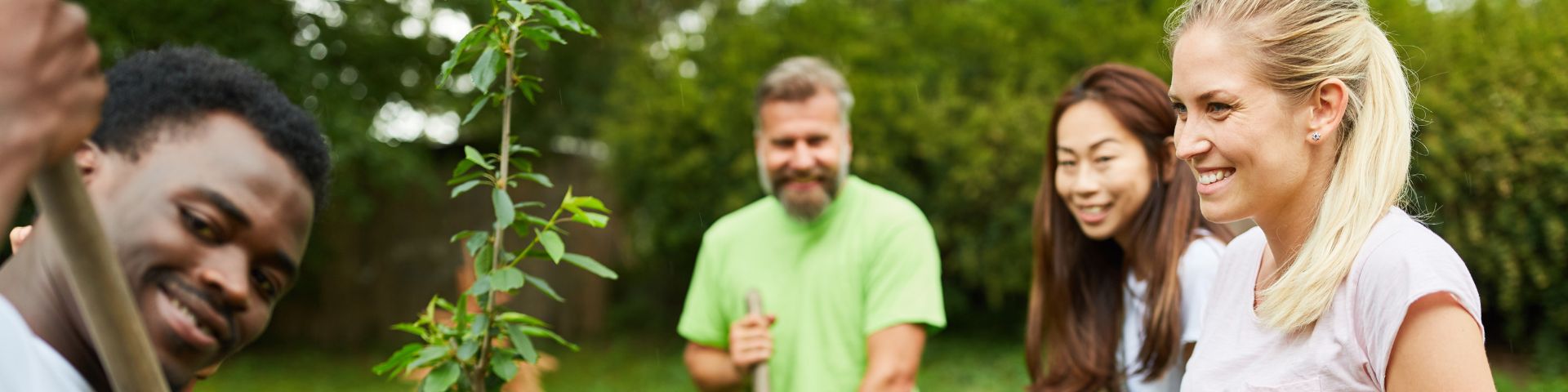 Vier Menschen unterschiedlicher Herkunft lächeln und pflanzen einen Baum im Garten