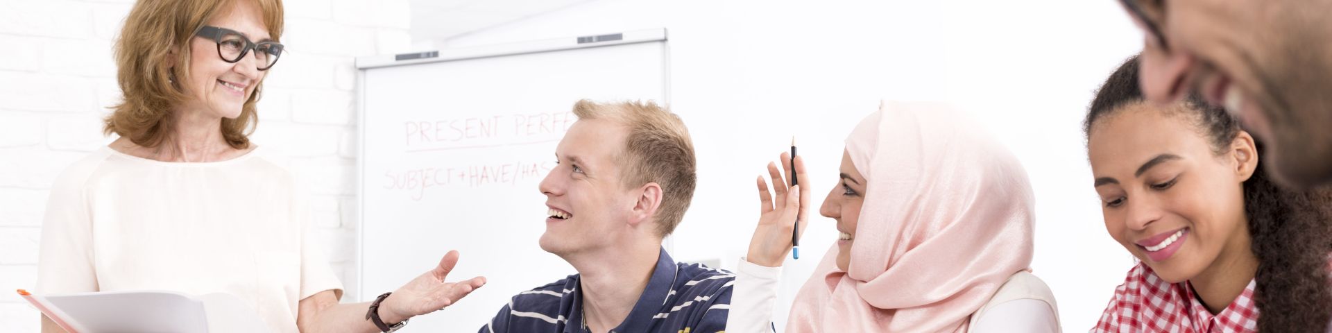 Spracherwerb für Migranten Fünf Menschen unterschiedlicher Herkunft sitzen an einem Tisch und diskutieren gemeinsam mit Papieren und Laptops.