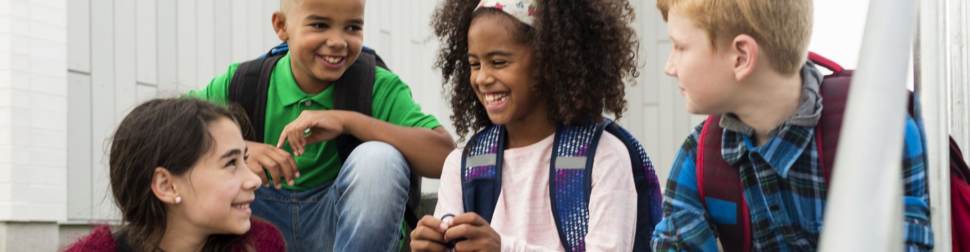 Vier Kinder mit Rucksäcken sitzen zusammen und lachen in einer Schulsituation