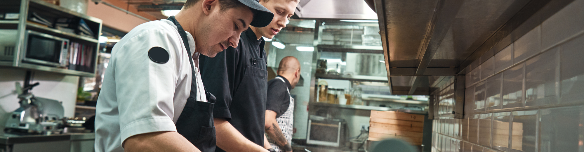 Leben und Arbeiten in Deutschland Drei Männer, in Küchenschürzen, die am Kochen sind.