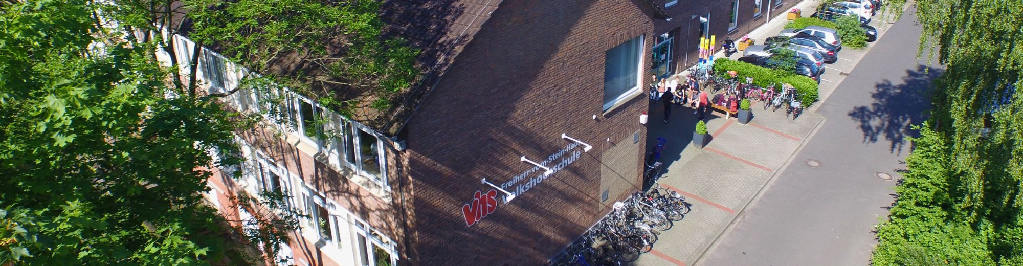 VHS-Gebäude Meppen: Blick auf ein Gebäude mit dem Schriftzug 'VHS' und Fahrrädern vor dem Eingang an einem sonnigen Tag