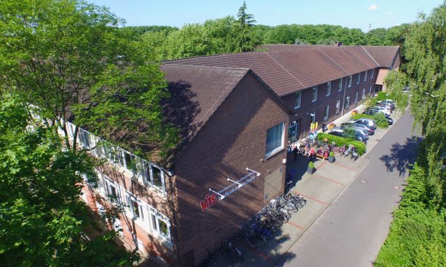 Meppen VHS-Gebäude Meppen: Langes, zweistöckiges Backsteingebäude mit roten Ziegeldach und Fahrrädern vor dem Eingang, umgeben von Bäumen und Parkplätzen